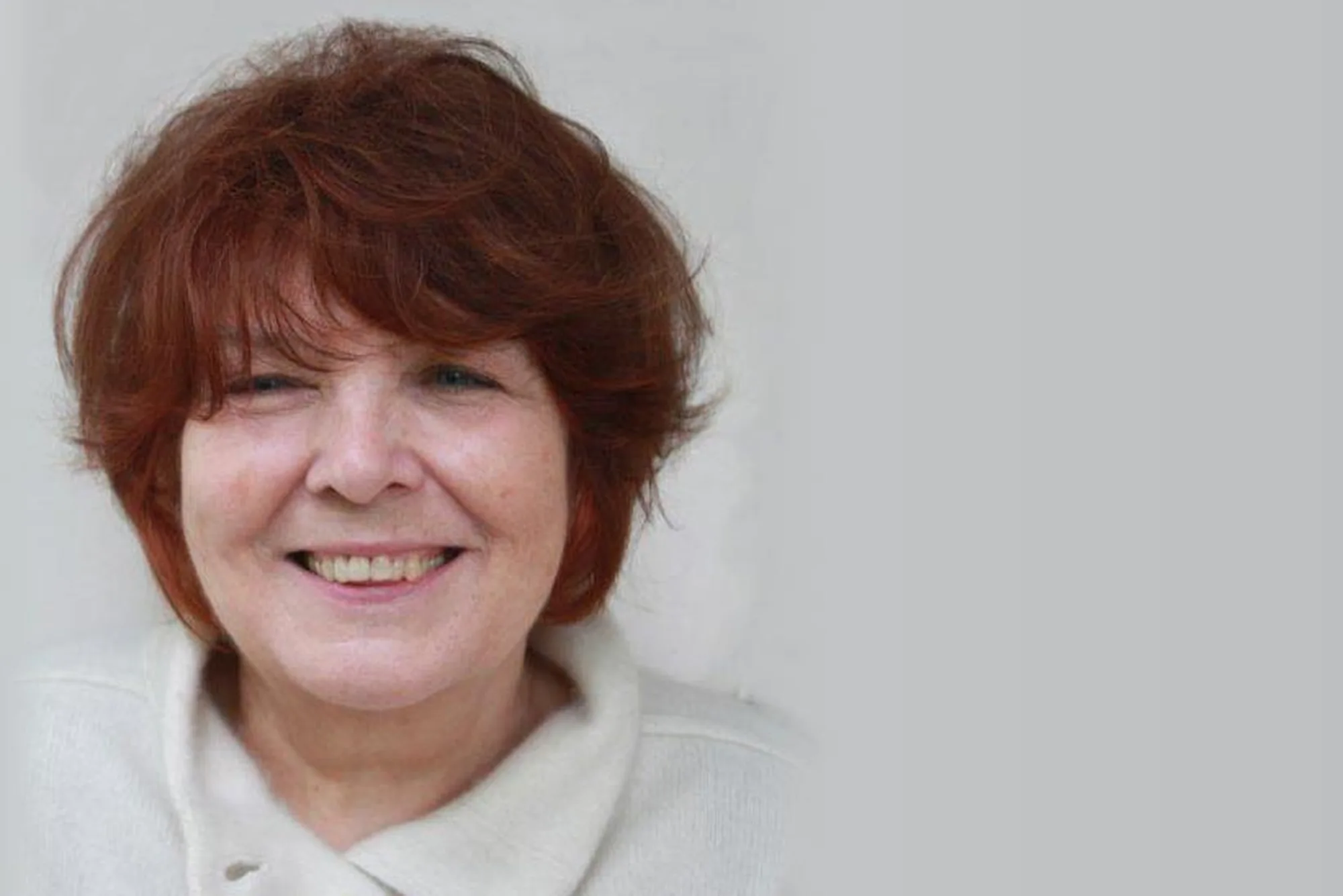 Porträt der Bildhauerin Jana Pfeifer mit kurzem rotbraunem Haar, lächelnd vor hellem Hintergrund
