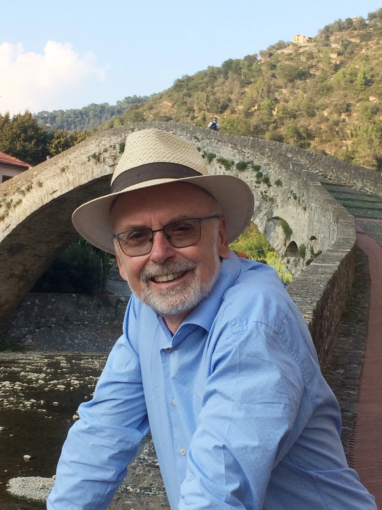 Bildhauer Reinhard Fescharek mit Strohhut und Brille vor einer alten Steinbogenbrücke