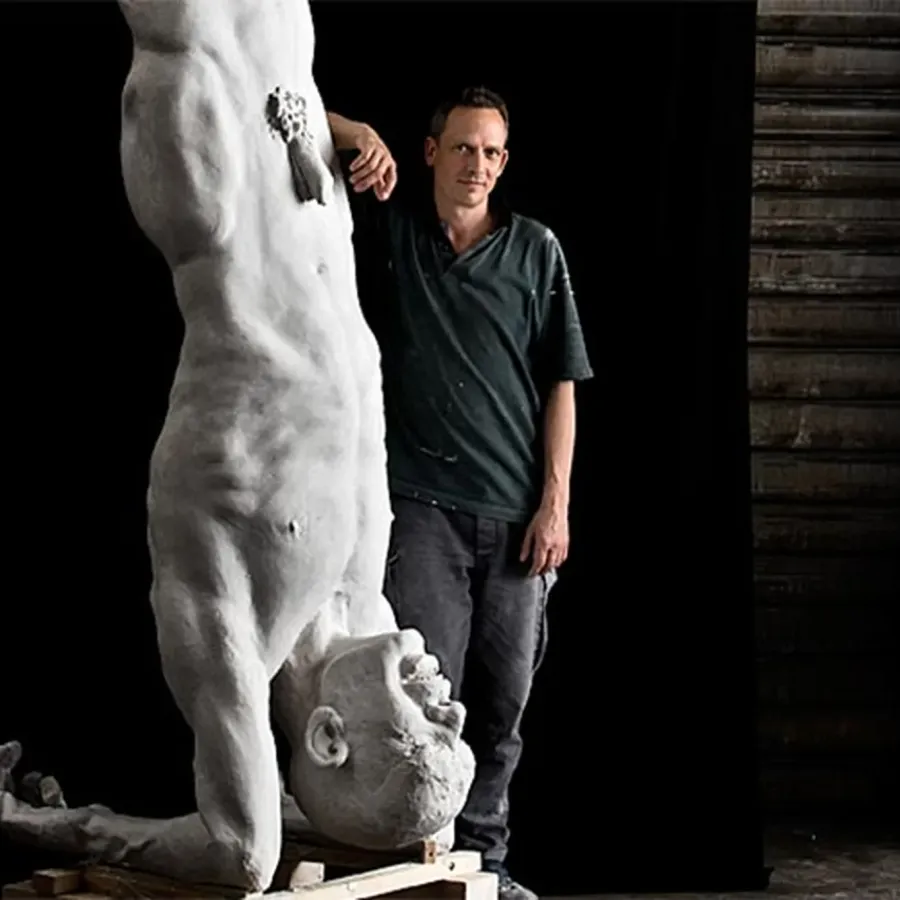 Sculptor Tilmann Krumrey next to a larger-than-life white figure standing on its head