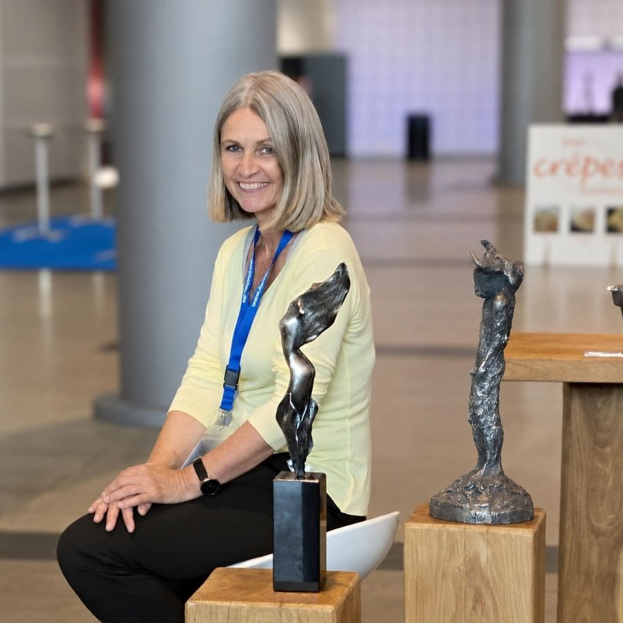 Frauke Deutsch, founder of BullionArt, sitting and smiling beside sculptures on wooden plinths at INVEST Stuttgart 2022