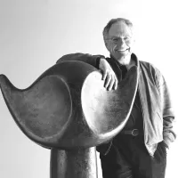 Sculptor Werner Pfändler smiling with his hand on a large curved sculpture, black-and-white photograph