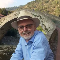 Bildhauer Reinhard Fescharek mit Strohhut und Brille vor einer alten Steinbogenbrücke